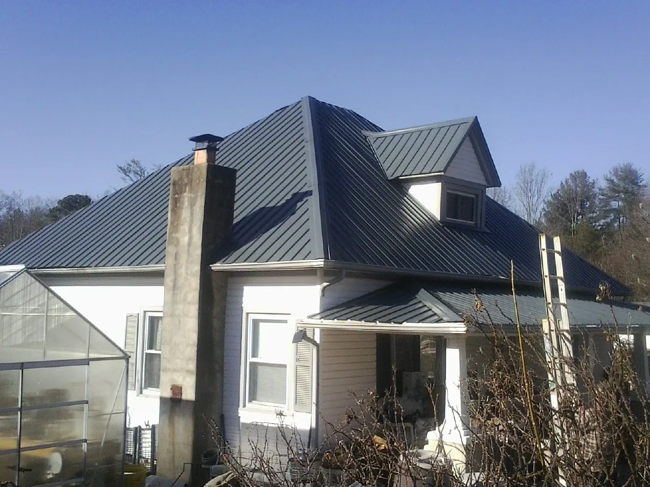 Dark blue standing seam metal roof on a white farmhouse with dormer — Slate & Tile Roof Repair by Roofing Brothers in Browning