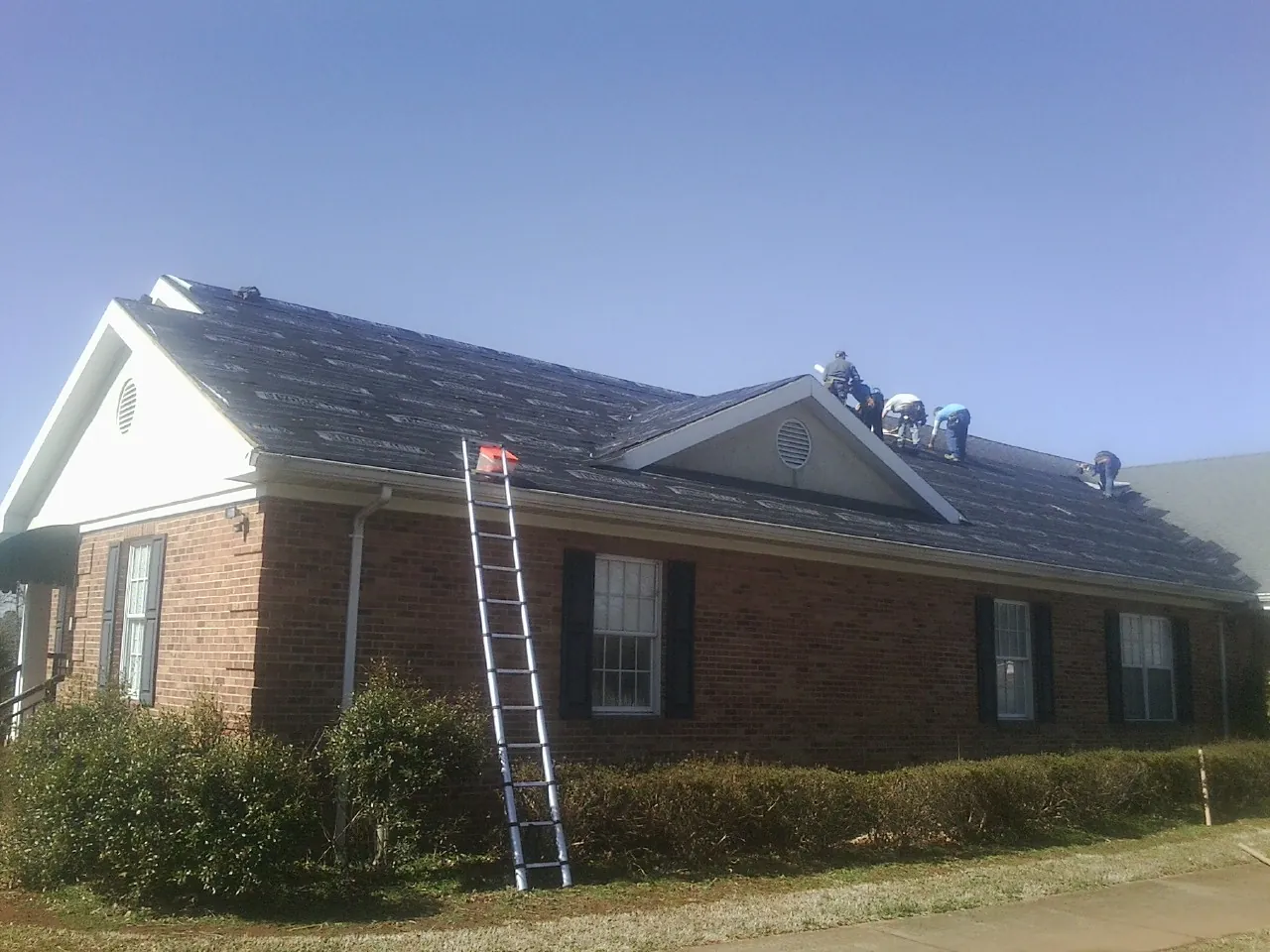 Crew tearing shingles off a brick ranch roof with a ladder set — Emergency Roof Repair work by our crew in Browning