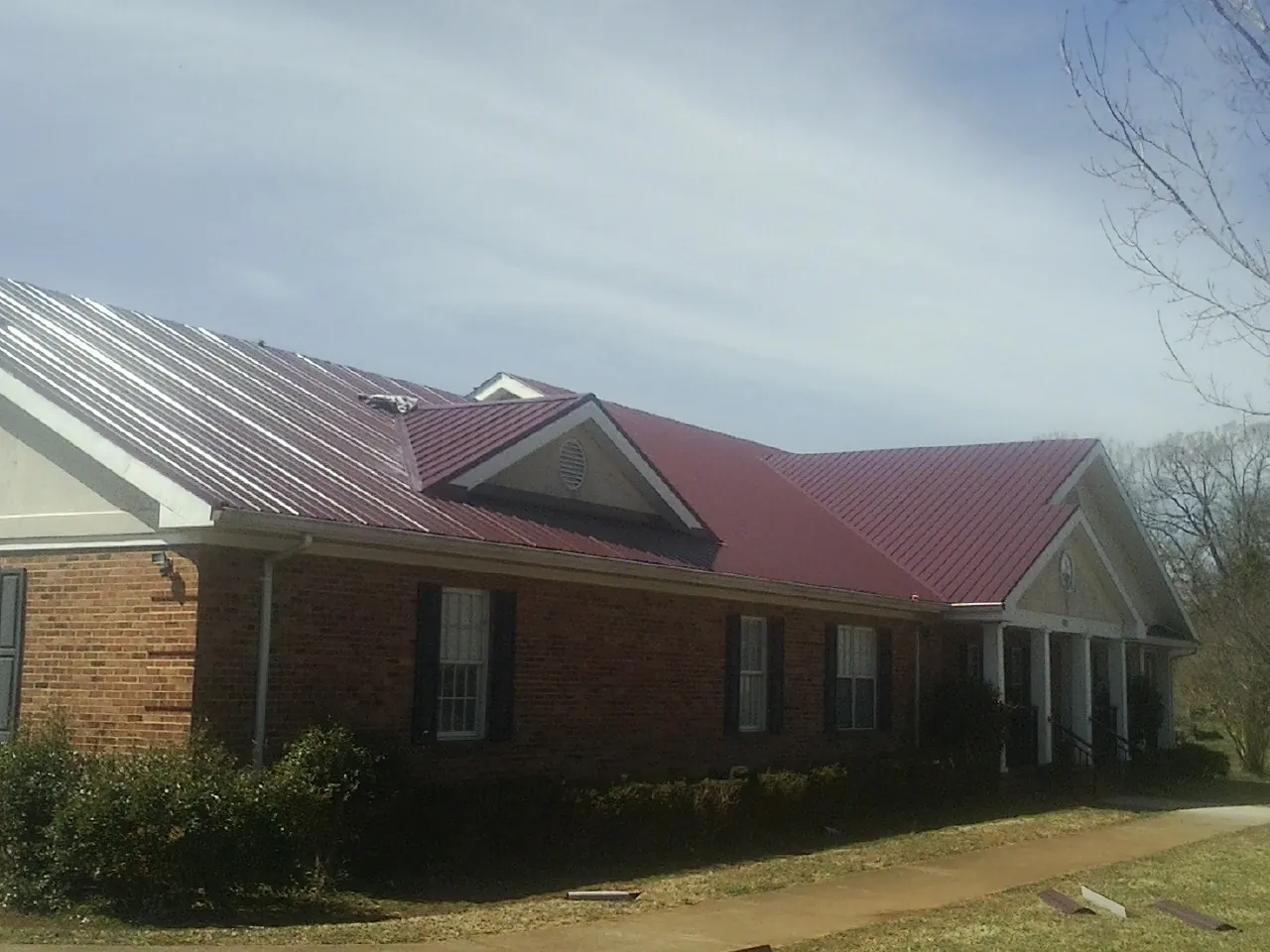 Red metal roof with gabled entries on a long brick building, from a Hail Damage Roof Repair job in Browning