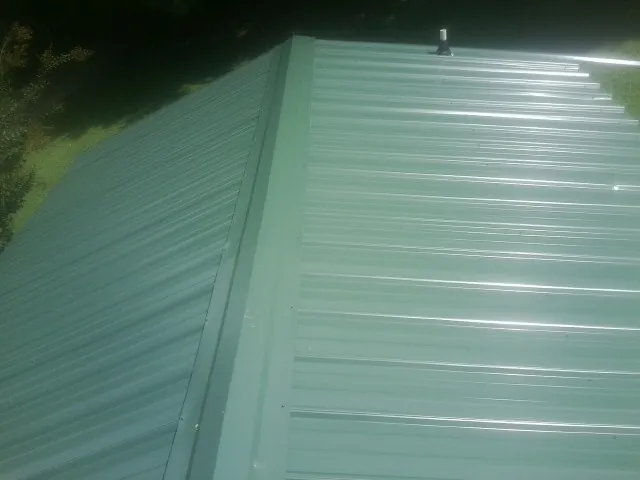 New green metal panels meeting at the ridge of a roof — Flat Roof Repair work by our crew in Browning