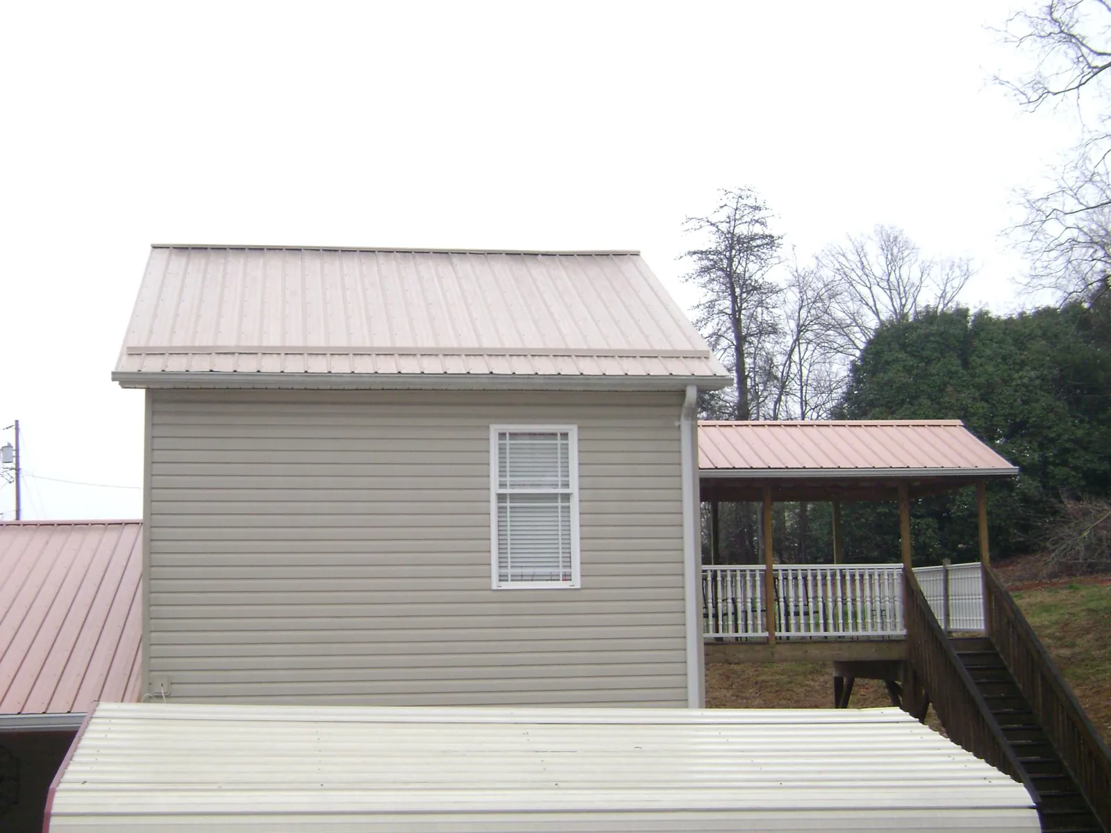 Tan metal roofs on a two story addition and attached porch, from a Roof Replacement job in Browning