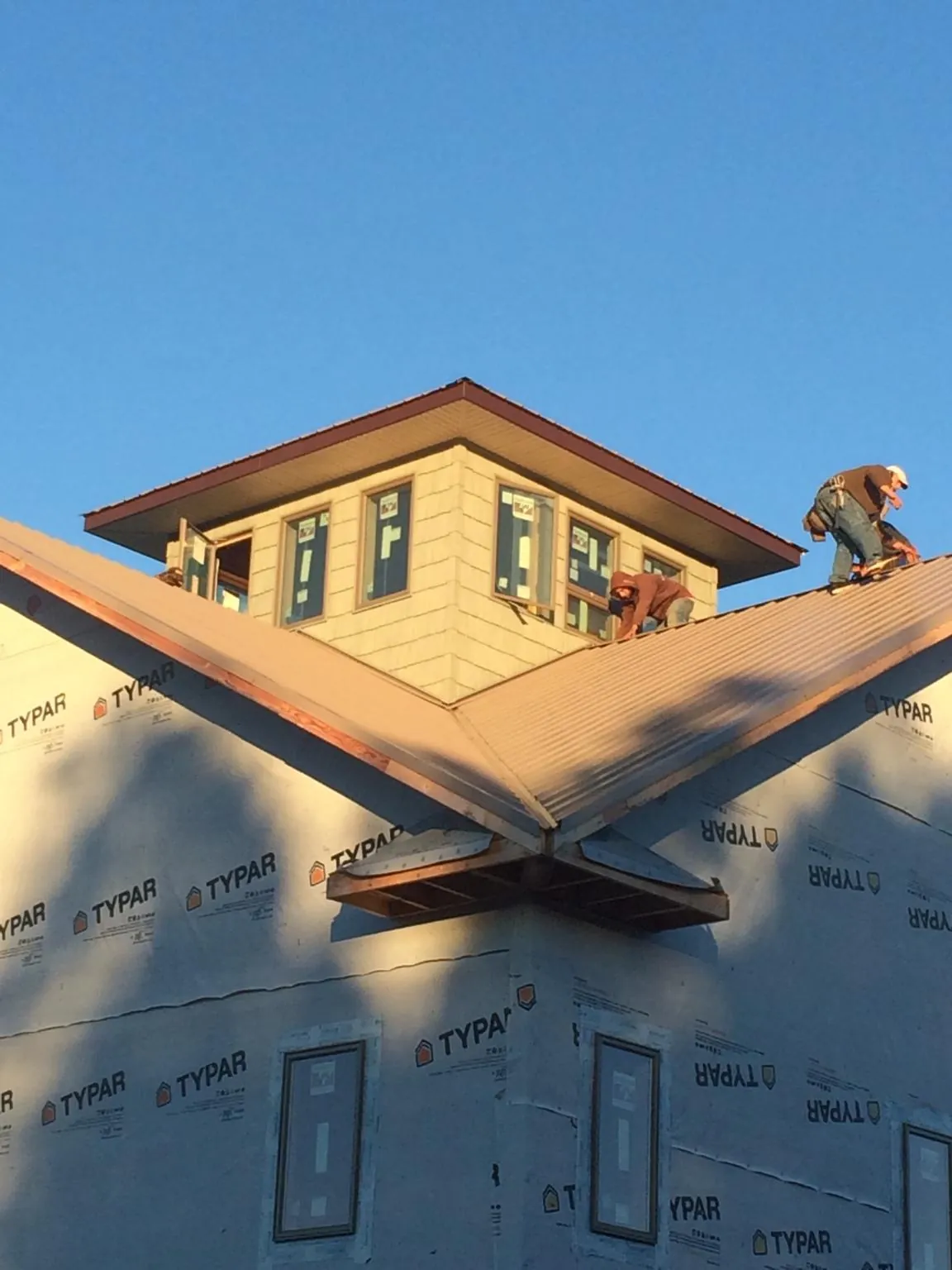 Roofers working around a rooftop cupola on a new metal roof at sunset — Roof Waterproofing in Browning by Roofing Brothers